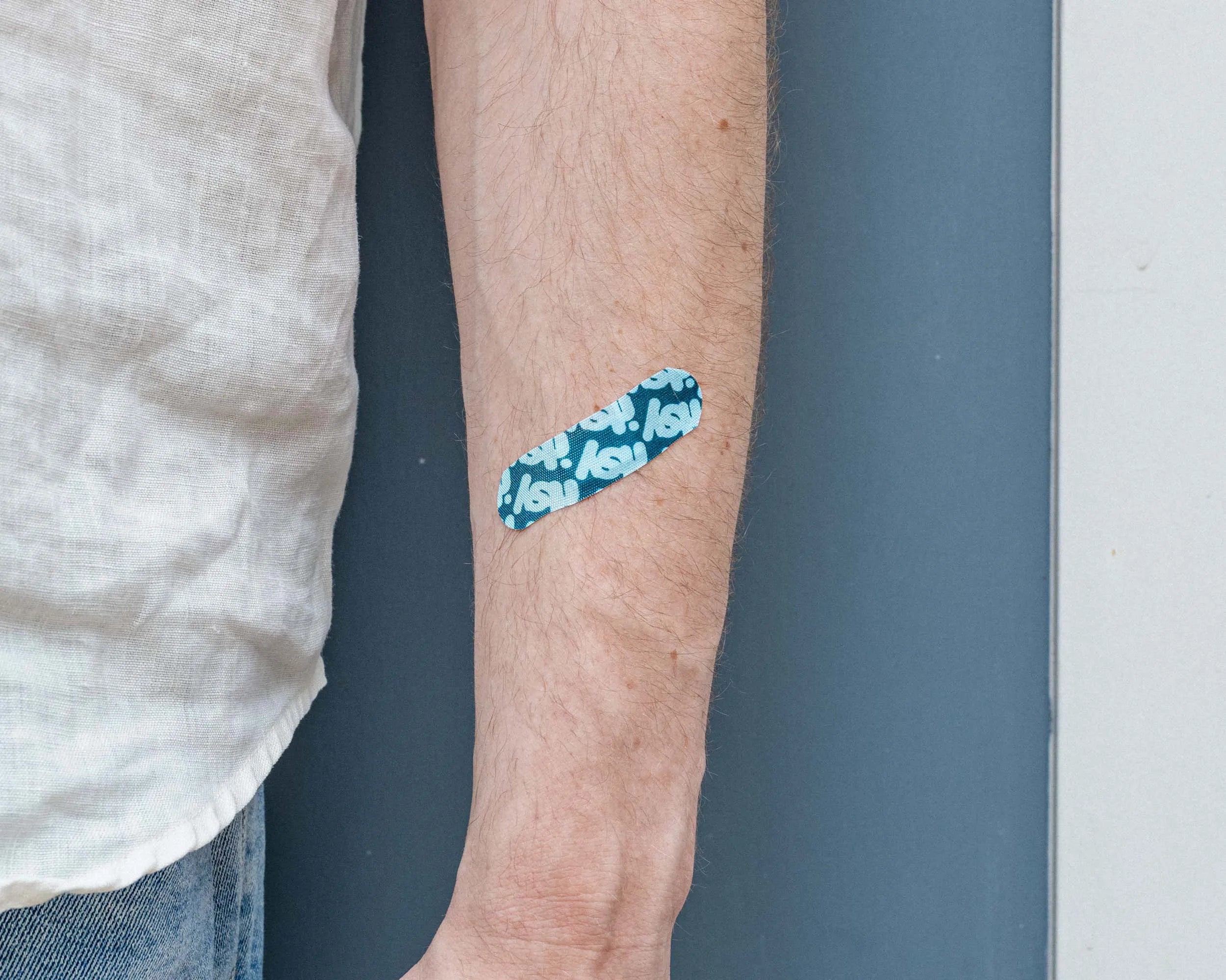 An itsy fabric bandage in the blue colorway worn on the inside of a forearm