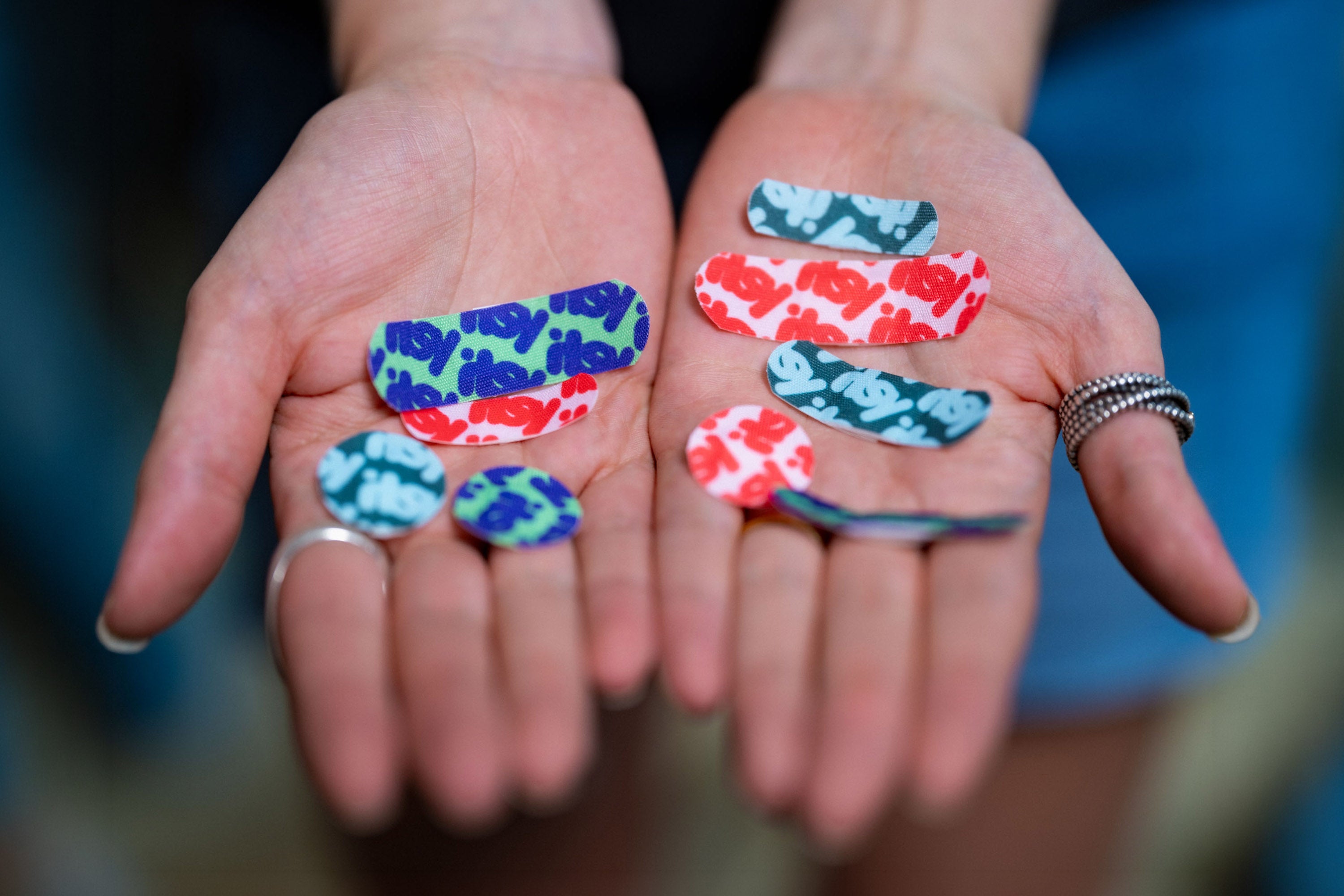 Two open hands holding an assortment of itsy fabric bandages in different sizes and colorways
